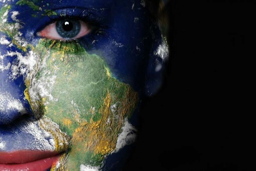 A woman's face with a world map painted on her face; South America on her left cheek.