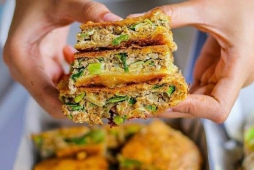 Hands holding three squares of Indonesian martabak, a dense pancake with different fillings.