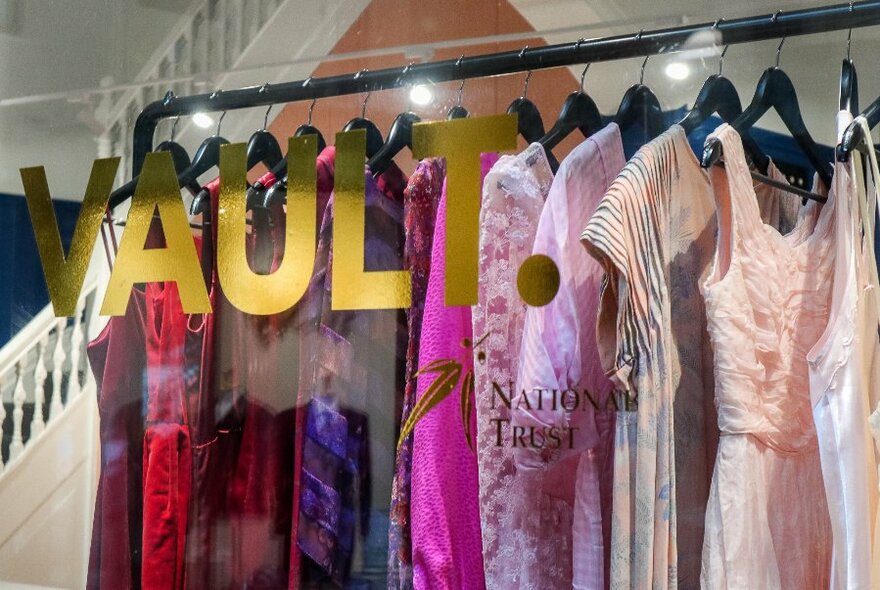 Racks of designer evening wear hanging on a rack behind a shop window with the words VAULT written in gold print.