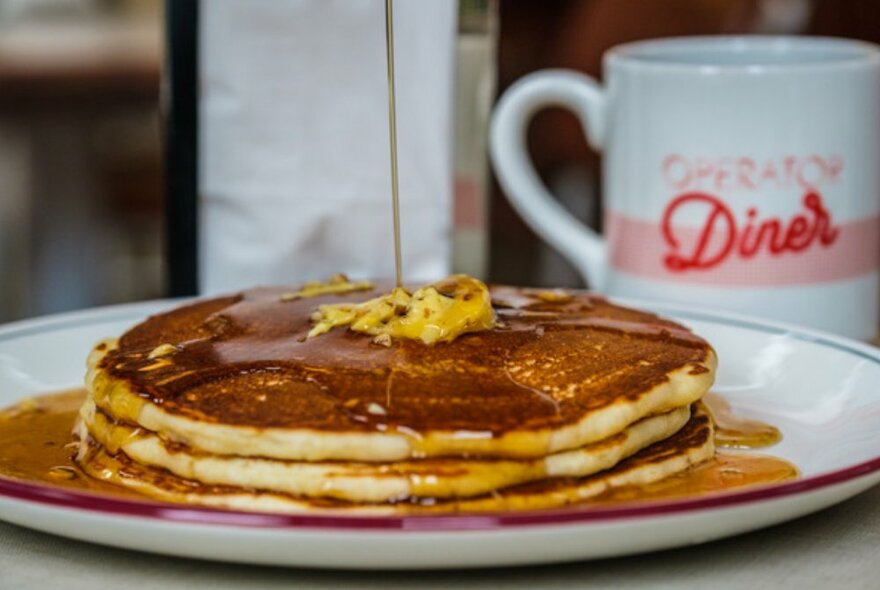 Pancake stack with butter and maple syrup being poured on top