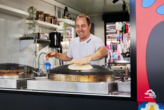 Chef preparing flatbread in a market kitchen stall.