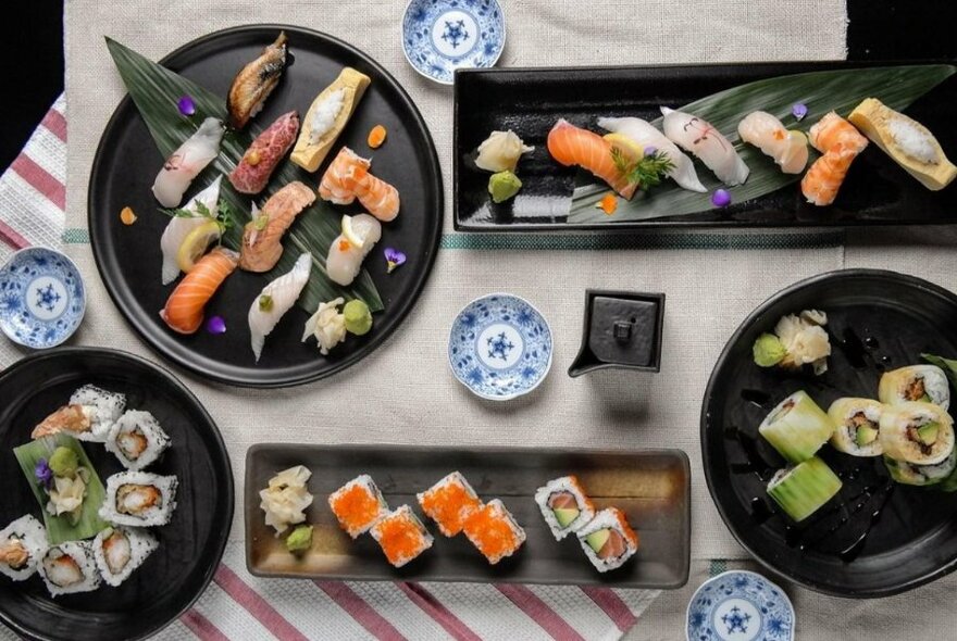 Overhead view of sushi and sashimi arranged on different sized black plates on a table.