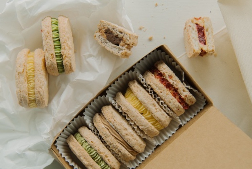A small box featuring four filled biscuits with more biscuits scattered around on paper. 