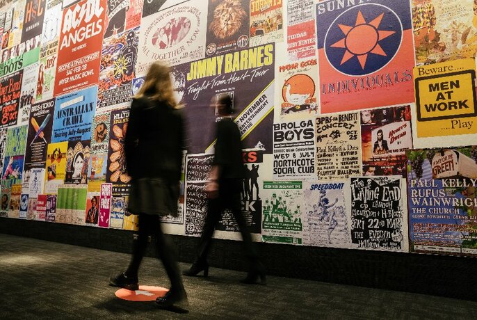 Two people, slightly blurred, walking along a wall of music posters.