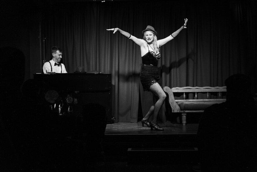 A black and white image of a woman performing in a cabaret setting with a pianist accompanying her. 