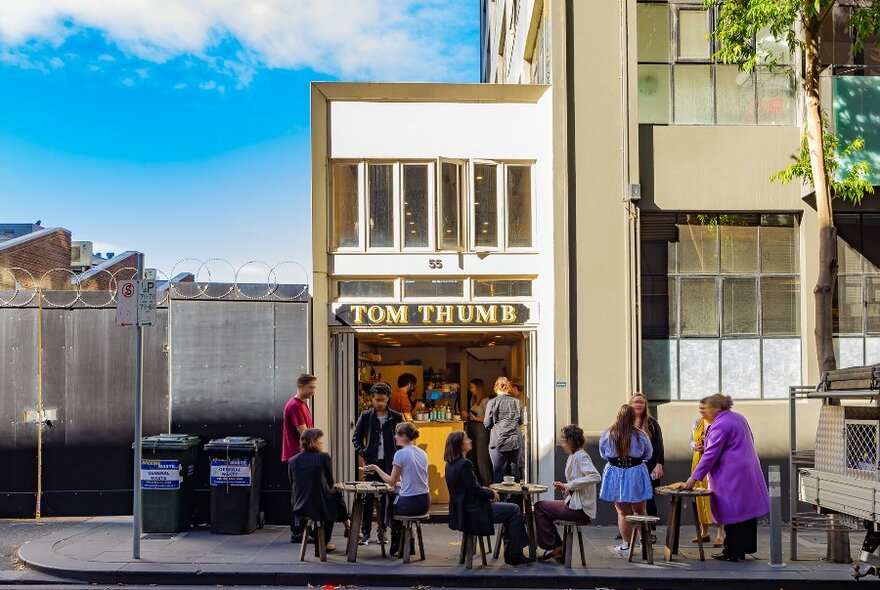 People sitting at tables outside a narrow two-story cafe. 