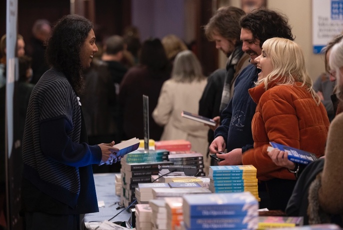People standing and laughing around a table stacked with books.