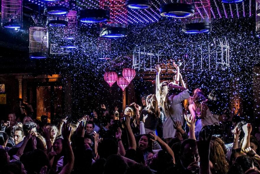 Inside a packed nightclub with people dancing under an illuminated ceiling. 