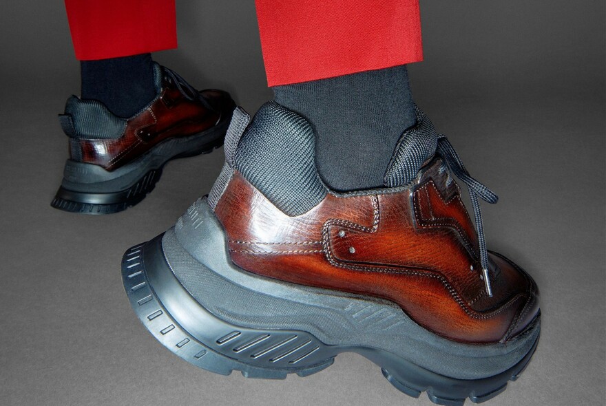 Detail of model wearing sneaker-style leather shoes and red trousers.