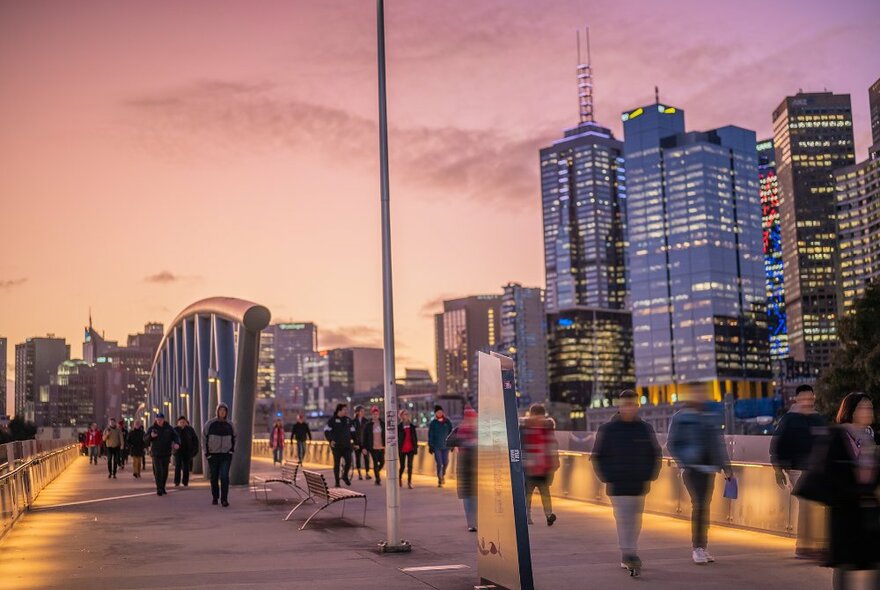 People walking over a city bridge at sunset.