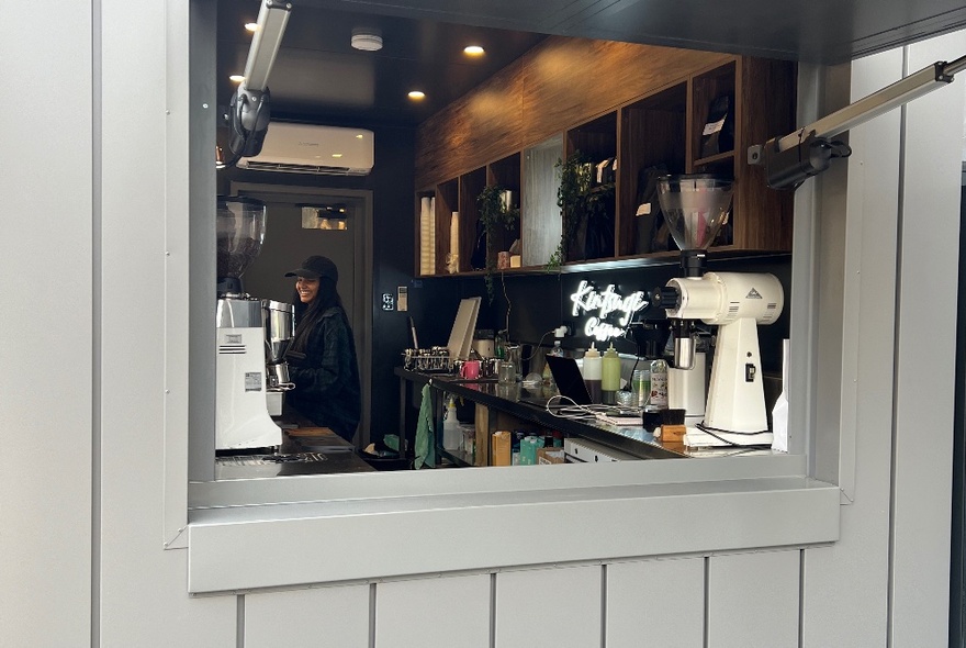 A serving window of a cafe, with a barista making a coffee inside.