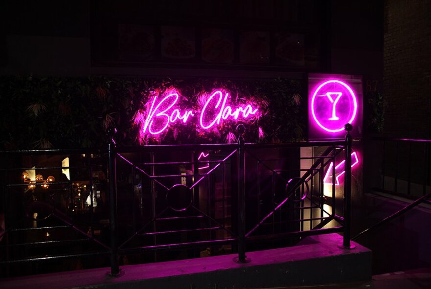 The exterior of a dark basement bar with a neon pink sign that says Bar Clara. 