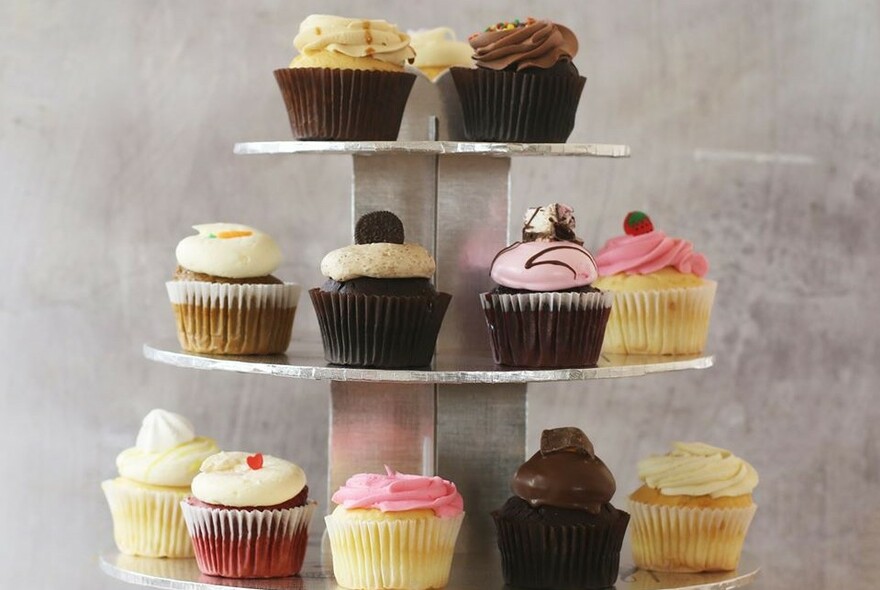 A three-tiered cake stand with vanilla, chocolate and strawberry cupcakes.