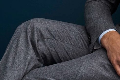 Crossed legs in grey marle suit, part view of arm with white cuff.