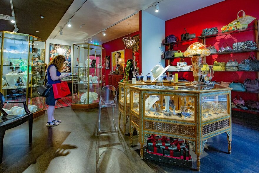 A woman browsing in an eclectic boutique with jewellery display cabinets and accessories on shelves.