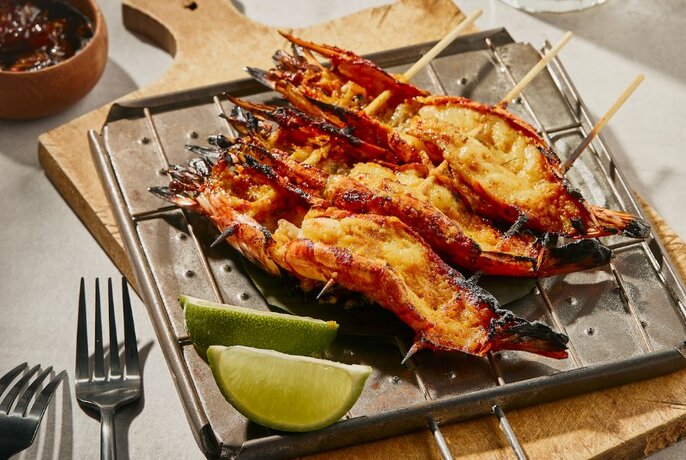 Grilled prawns on skewers with lime wedges.