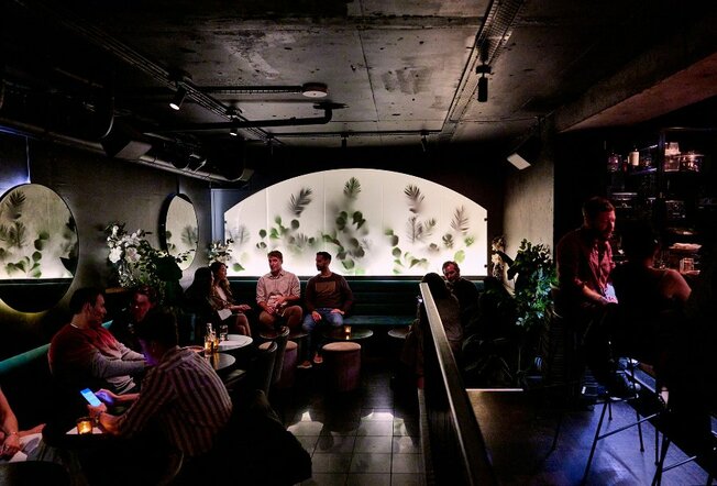 A busy bar with a feature wall of leaves behind a frosted window. 