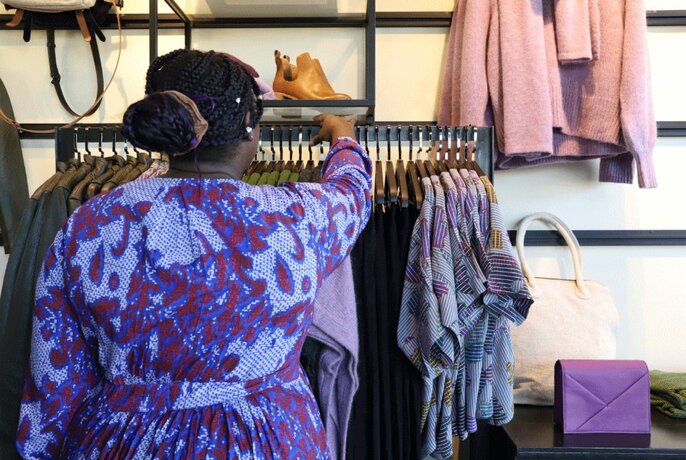 Rear view of a person wearing a patterned Elk dress adjusting clothing hanging on the display rack in store.