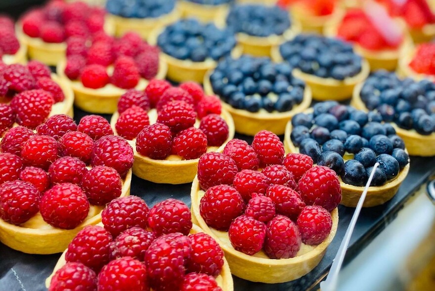 A tray filled of tarts topped with fresh raspberries and blueberries.