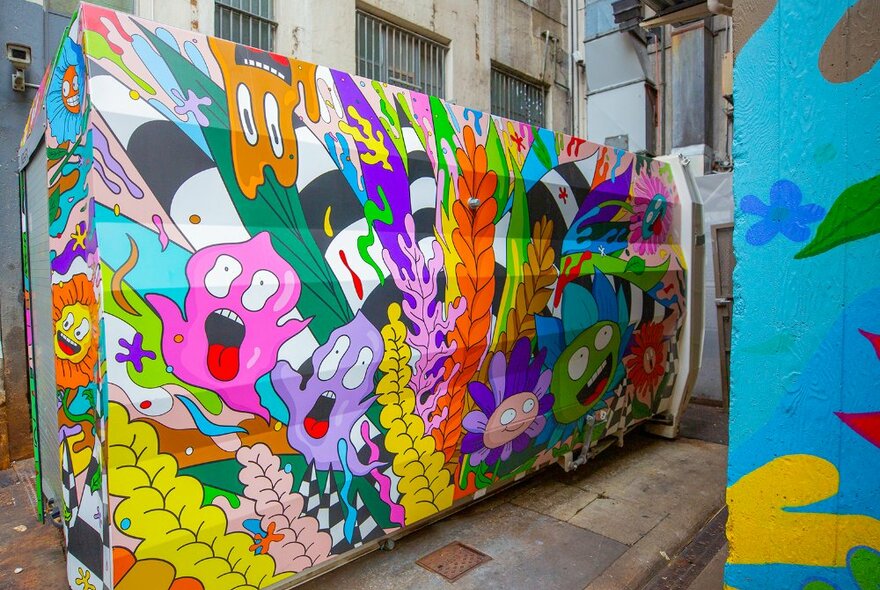 A rubbish compactor covered in colourful characters.