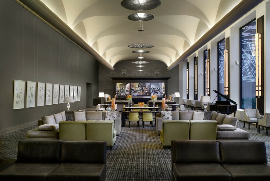 Sofi's Lounge with groups of grey chairs, grey carpet and walls, grand piano, food bar at end under white coffered ceiling.