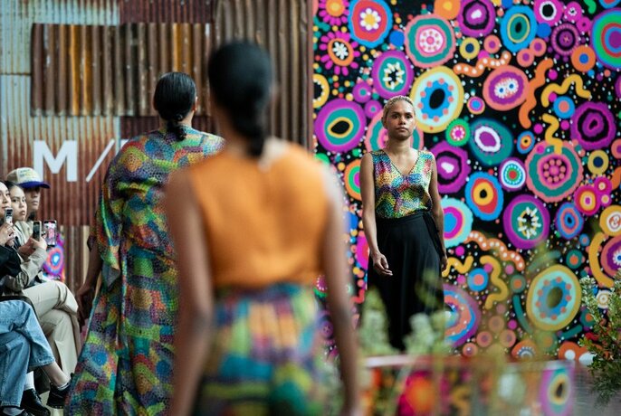Blurred motion image models on a catwalk with a bright design in the background. 