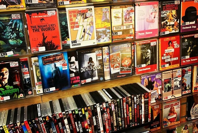 Shelf in a shop filled with DVD movies, stacked face out and vertically.