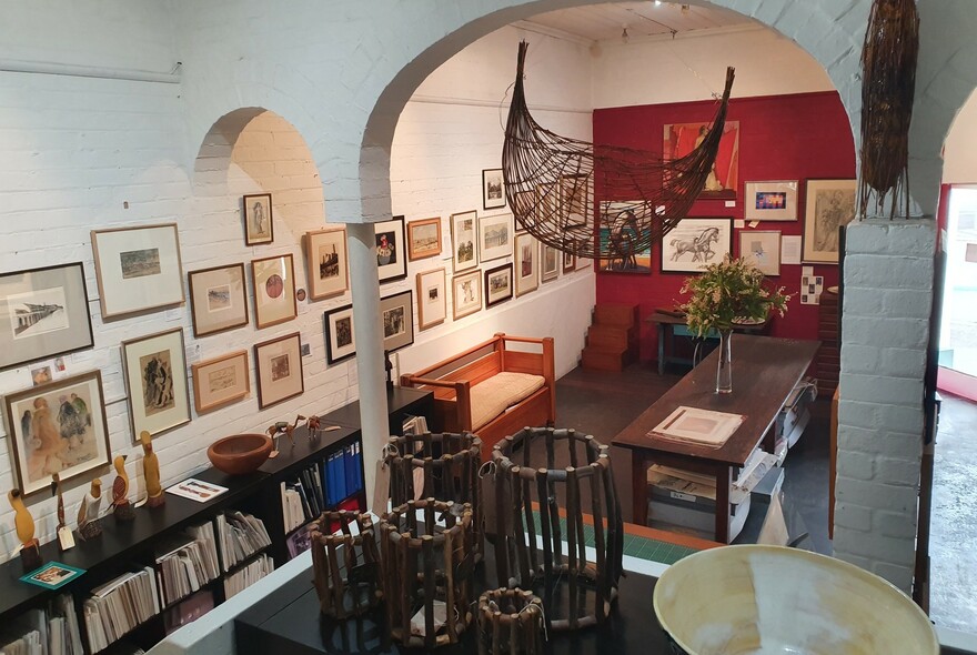 Gallery space displaying framed art on the walls, and small sculptures on shelves and tables.