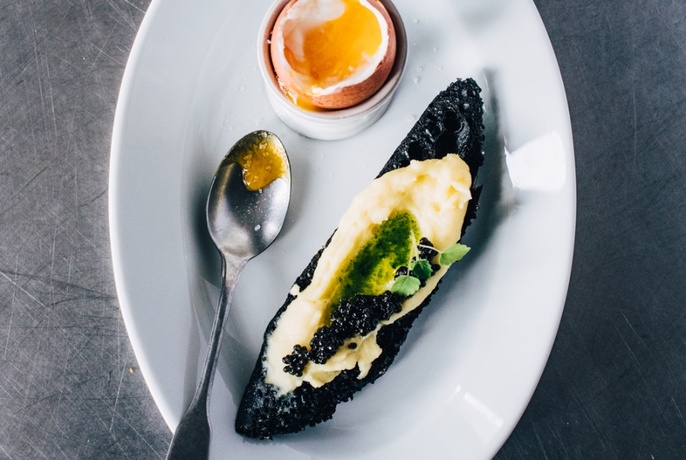 An oval white plate with a soft boiled egg, rye bread and caviar.
