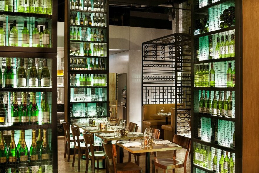 Interior of Platform 270 restaurant showing a row of dining tables set for service, surrounded by shelves filled with green glass bottles of wine and sparking.