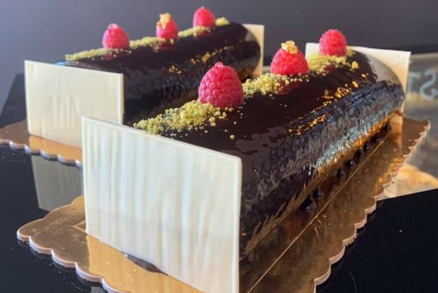 Two chocolate logs on gold foil topped with pistachios and raspberries.