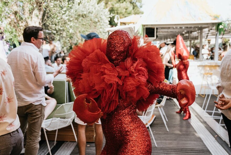 A performer in a red catsuit on board a boat with people in the background.