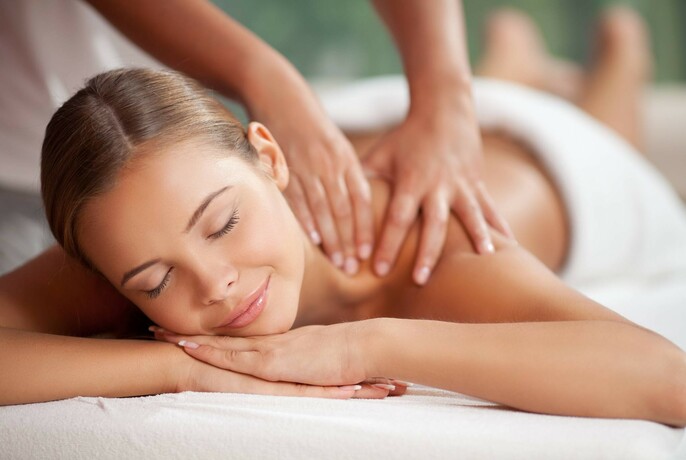 Woman lying on her front and smiling while hands massage her shoulders