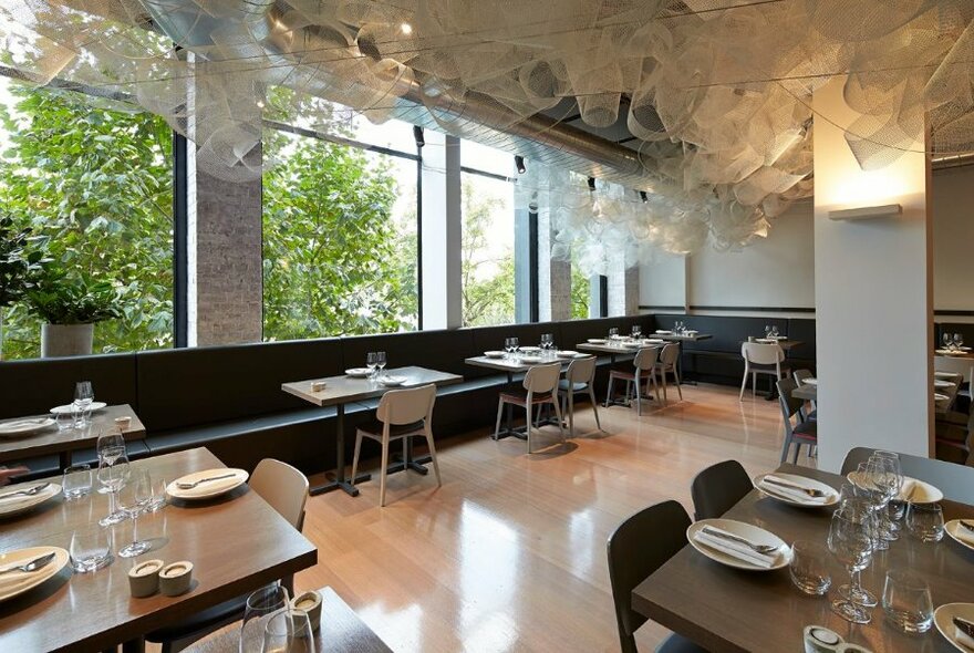 Restaurant interior with tables against large windows, floating white chiffon fabric on ceiling.