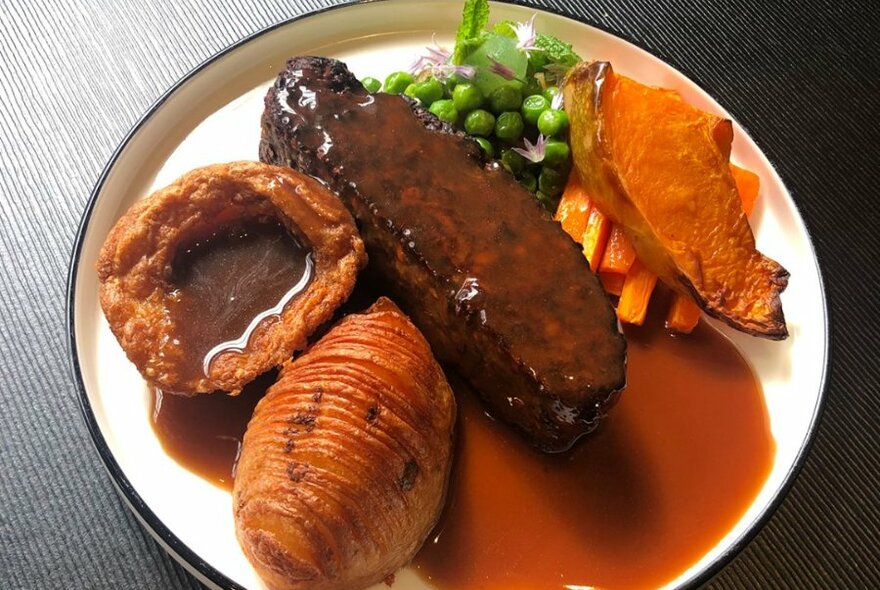 A nut roast dish with gravy, hasselback potato, vegetables and a Yorkshire pudding.