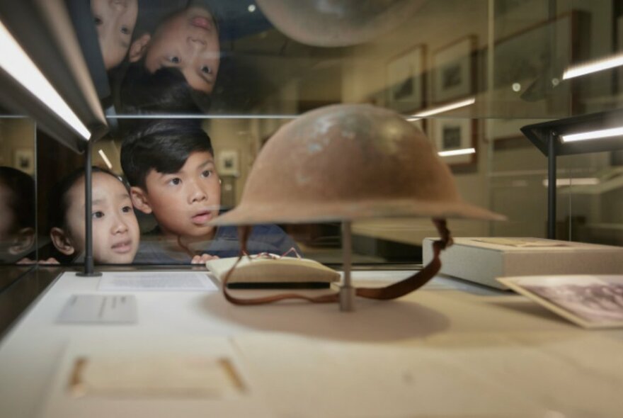 Children looking into a glass display case featuring a wartime metal helmet and artefacts.