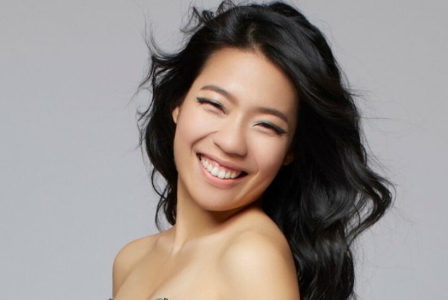Head and shoulders of a smiling woman, the pianist Joyce Yang, her long dark hair cascading over her bare shoulders.