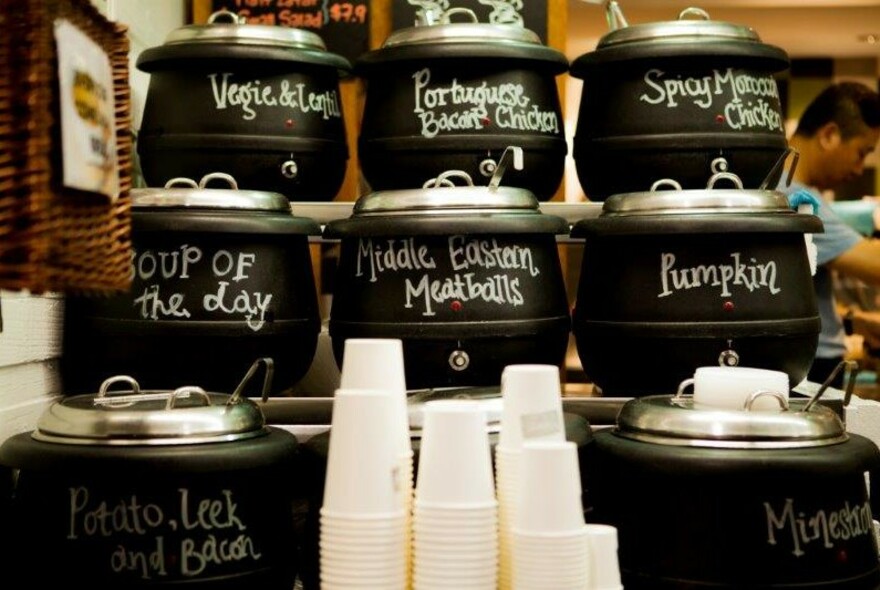 Black pots of soup lined up with takeaway cups.