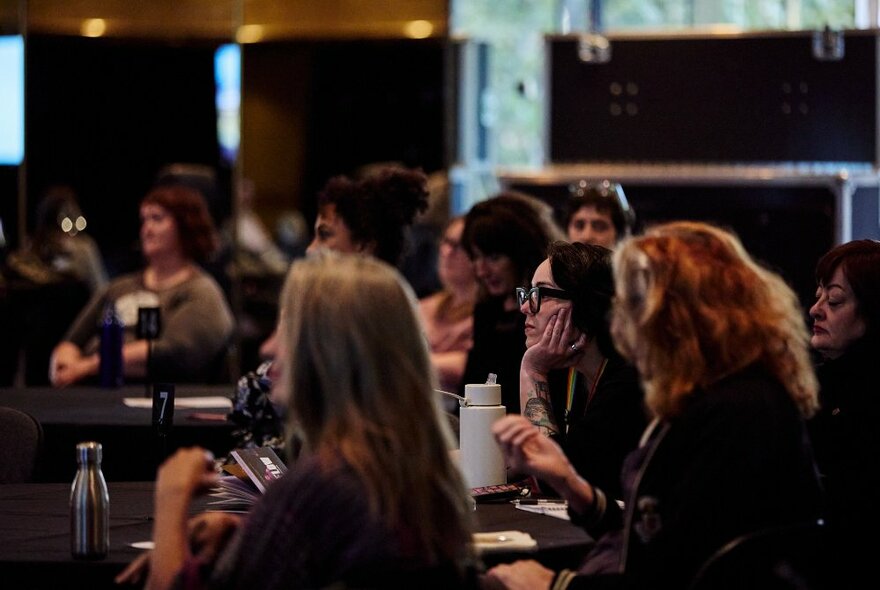 A room with people listening to a presentation, sitting at tables. 