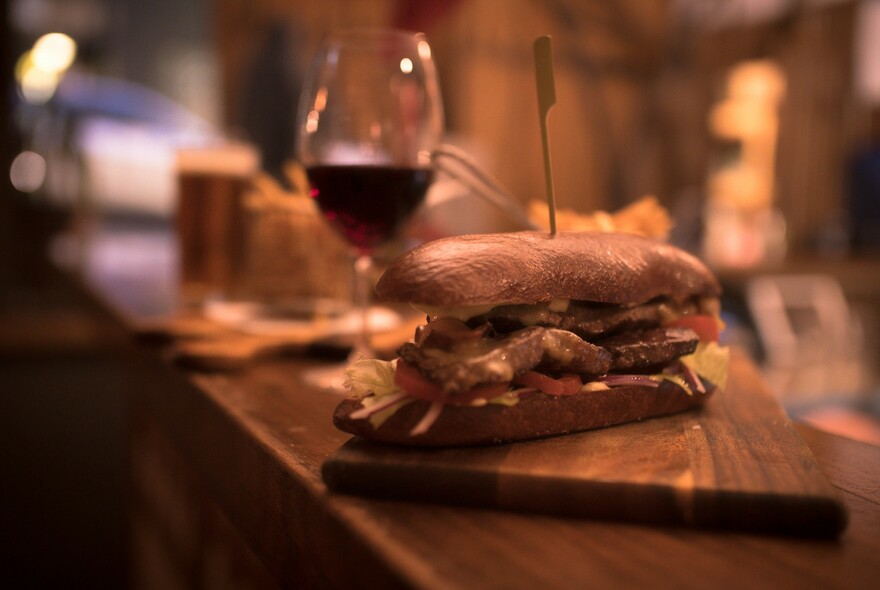 Bar counter with a glass of red wine and a panini on a wooden board.