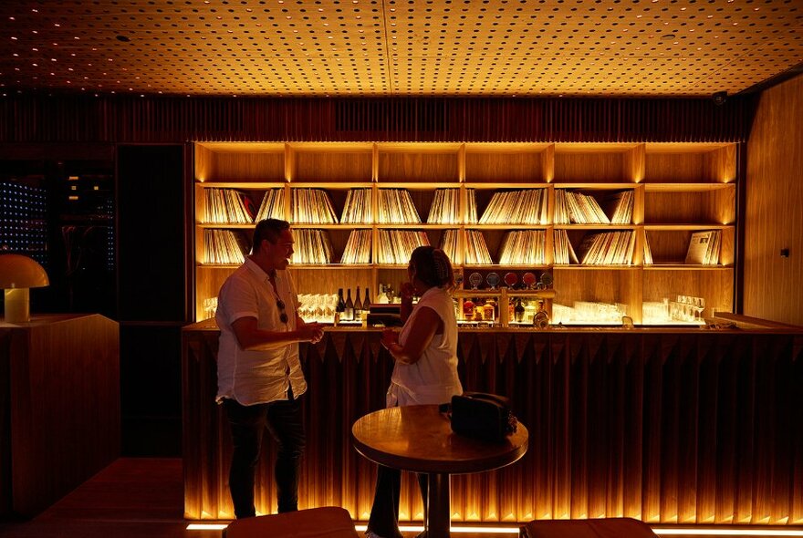 A couple in a dark bar with glowing shelves of records. 