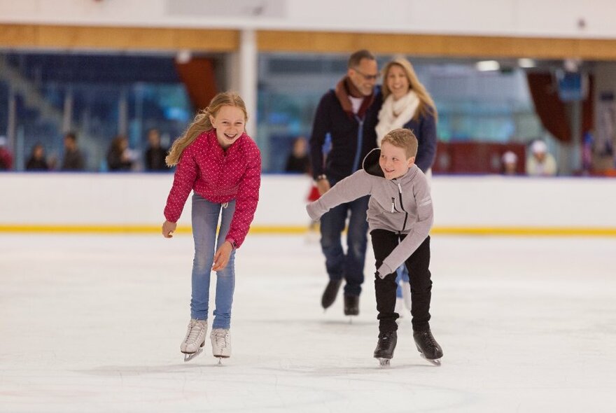 Two children ice skating with their parents behind them