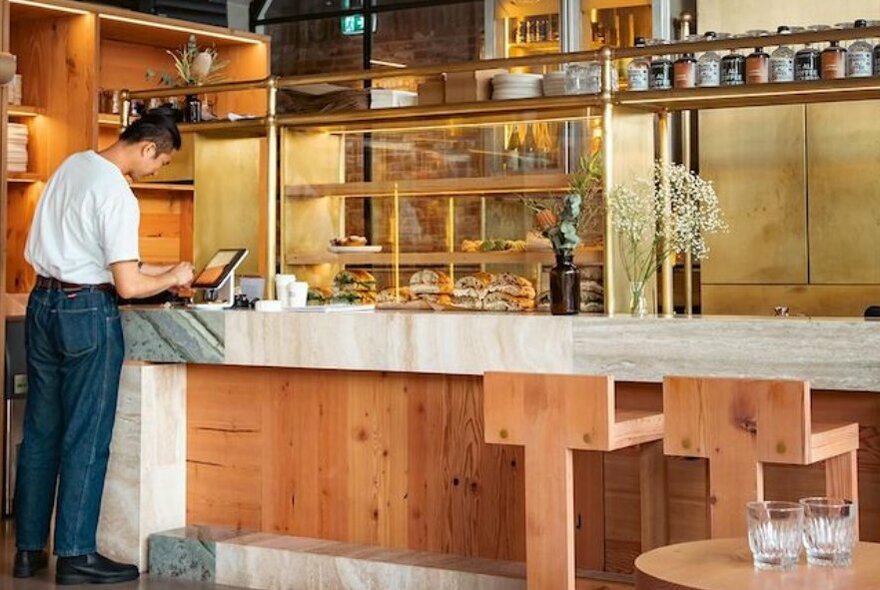 Cafe interior with person standing at a concrete bench with wooden shelves and seating.