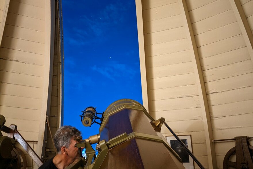 A man looking into the eyepiece of a large telescope, pointed towards the night sky at the Melbourne Observatory.