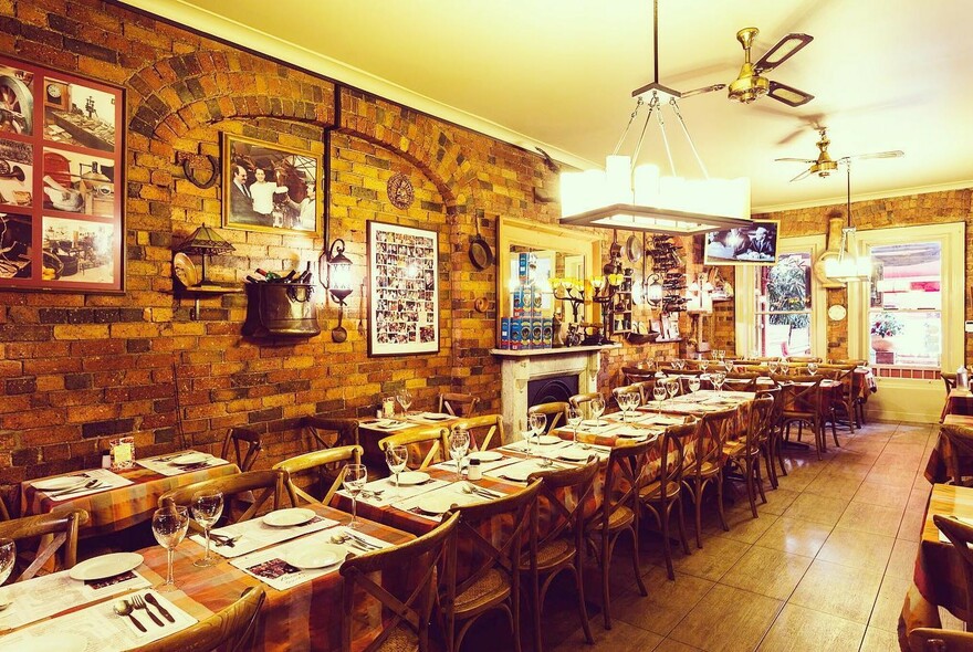 Restaurant interior with long row of tables and chairs against a highly decorated brick wall.