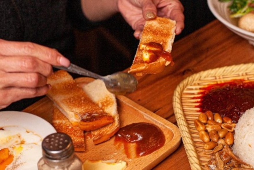 Hands using a teaspoon to smear sambal oelek onto a slice of toast.