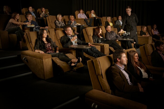 Audience enjoying a Gold Class cinema experience in reclining armchairs with food and drinks.