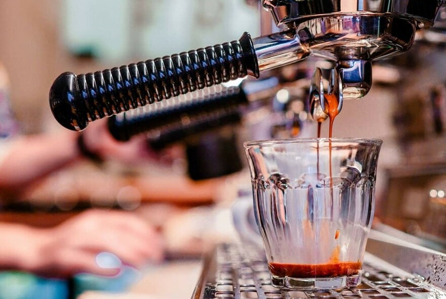 Side view of a coffee machine, with espresso coffee dripping into a glass.