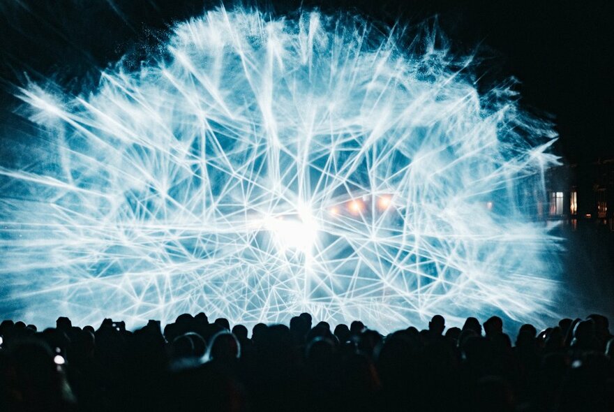 Crowds watching a light show with a web of geometric blue light beams.