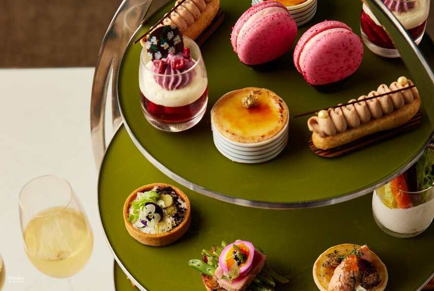 Two-tiered olive green plate of petit-fours and small desserts, glass of champagne to left.